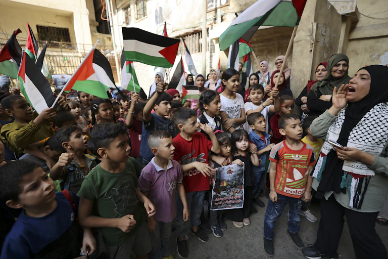 Une femme crie quelque chose devant des enfants portant des drapeaux palestiniens
