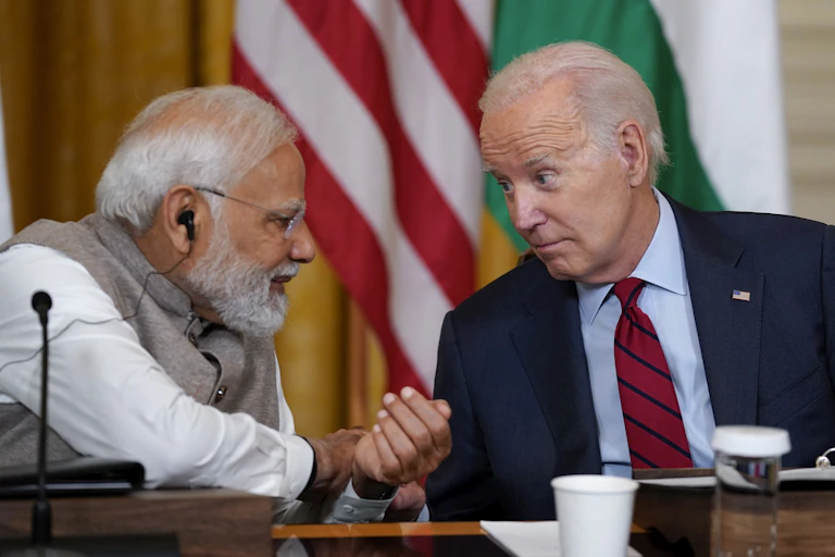 Elderly man in a dark suit talking to elderly man in Indian clothing