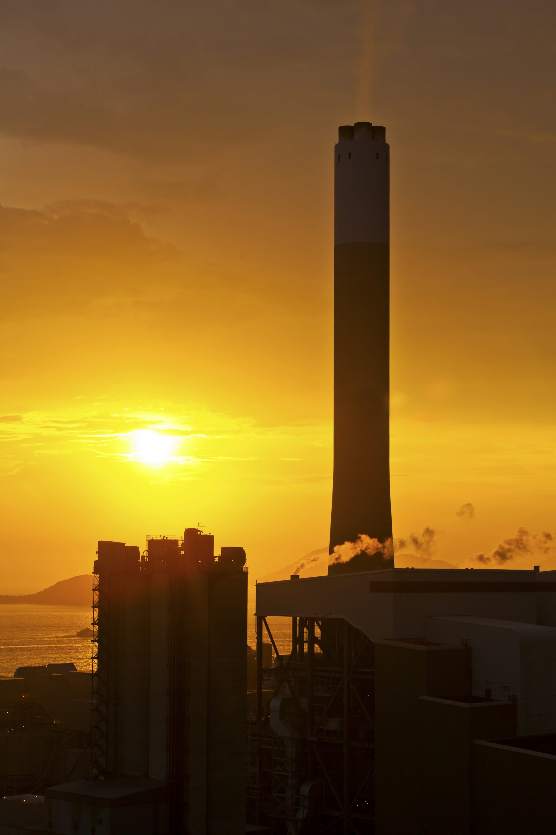 Chaminés de uma fábrica tendo como pano de fundo o pôr do Sol