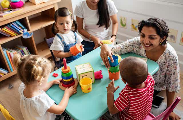 Two women with nursery-age children, at a table with stacking toys.