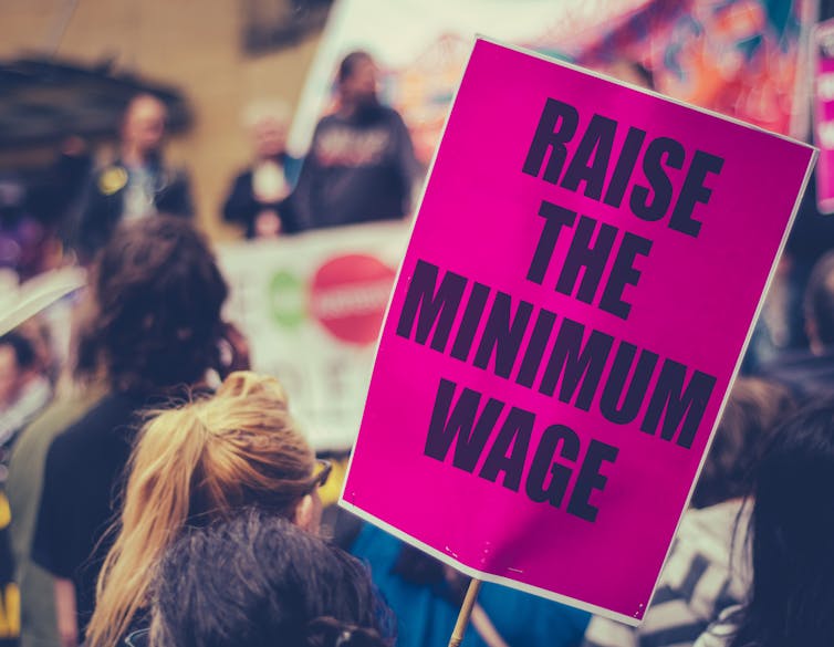 Person at a protest with a pink sign that says raise the minimum wage.
