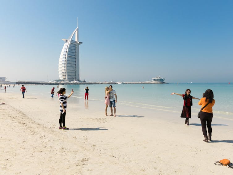 A Dubai beach with women taking selfies by the sea.