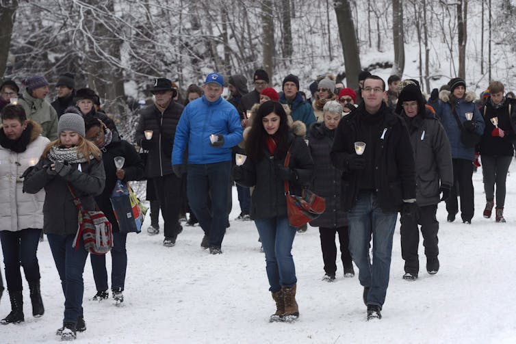 People seen walking with candles through a snowy area.