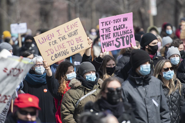 People seen at a demonstration, one with a pink sign that says 'tick tock...the kilings must stop.'