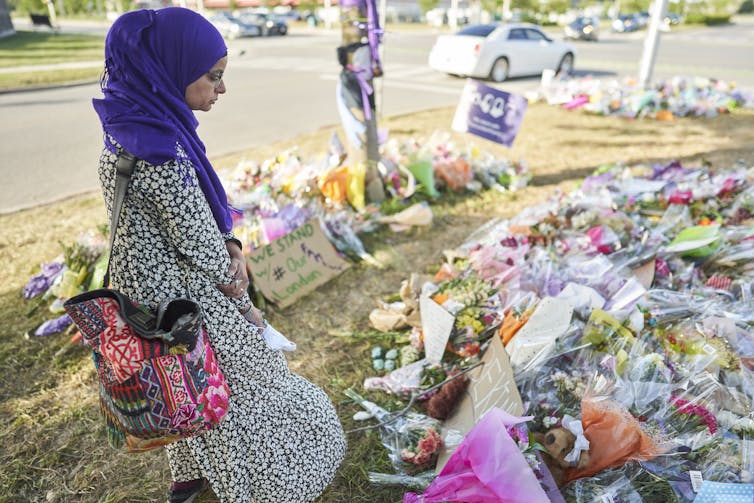 A woman wearing a hijab looks at a memorial of flowers on the ground.