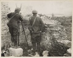 Una fotografía en blanco y negro de dos soldados de espaldas vigilando tras un muro.