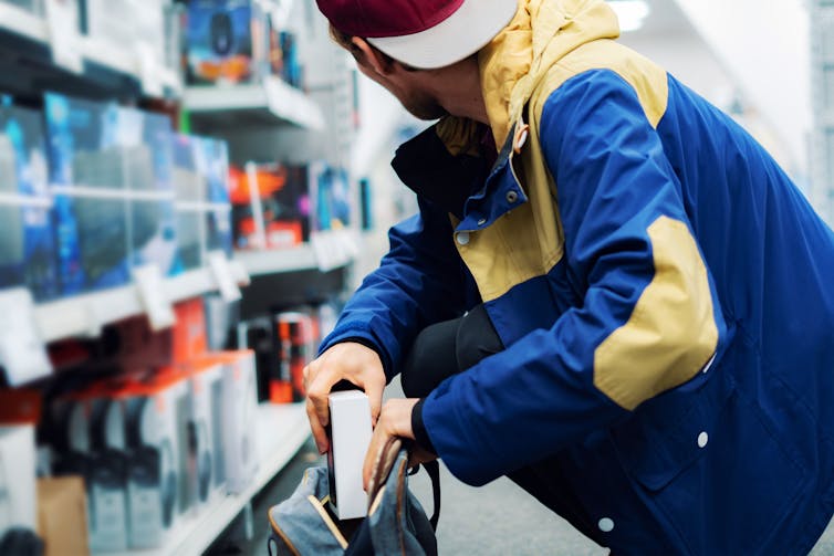 A man in a supermarket surreptitiously placing a product in a backpack.
