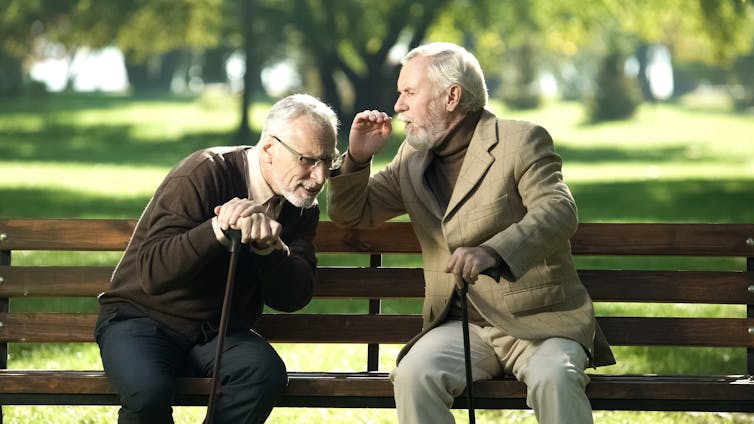 Two older men on a park bench, on of whom is straining to hear the other speaking