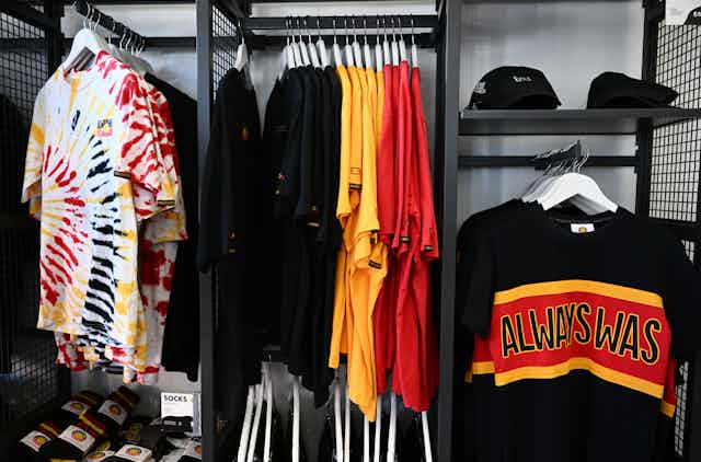 An image from the Indigenous-run Clothing the Gaps store. There are shirts in Aboriginal flag colours and black caps with the Aboriginal flag on them.