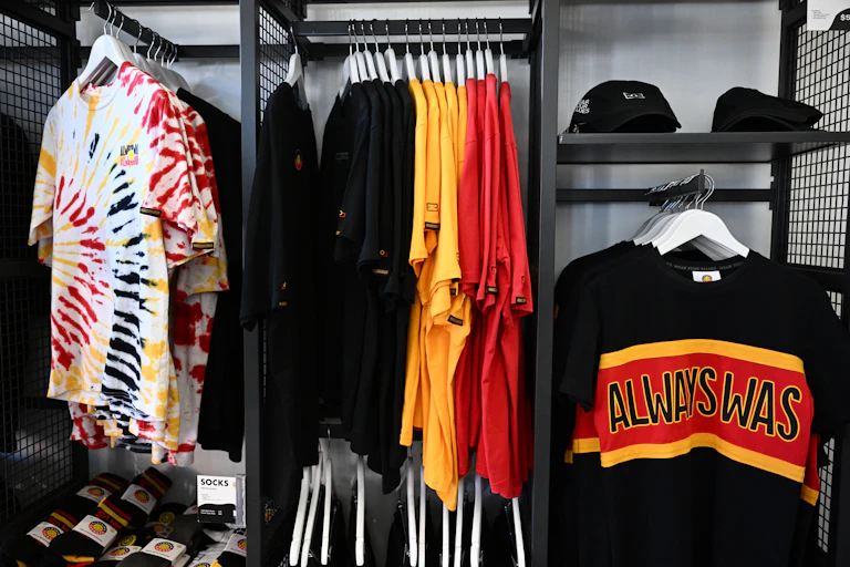 An image from the Indigenous-run Clothing the Gaps store. There are shirts in Aboriginal flag colours and black caps with the Aboriginal flag on them.