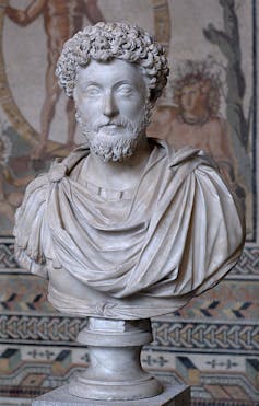 A bust of a man draped in robes, with short, curly hair and a beard.