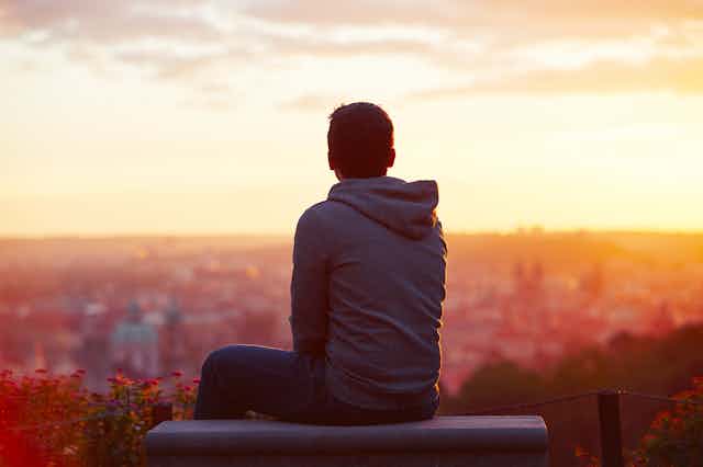 A young man in a hoodie looks out onto the sunrise