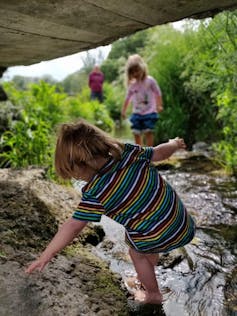Children climb near a stream, while an adult watches on.