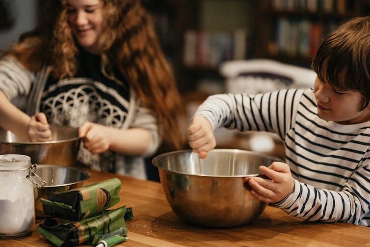 two children at kitchen bench stirring in mixing bowls