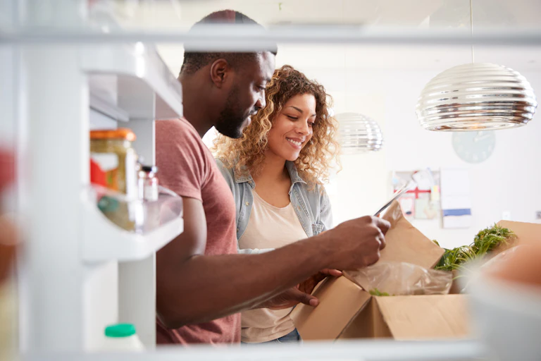 couple unpack meal kit box by fridge