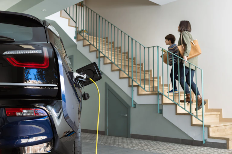 mother and son walking up stairs from garage with EV charging in foreground