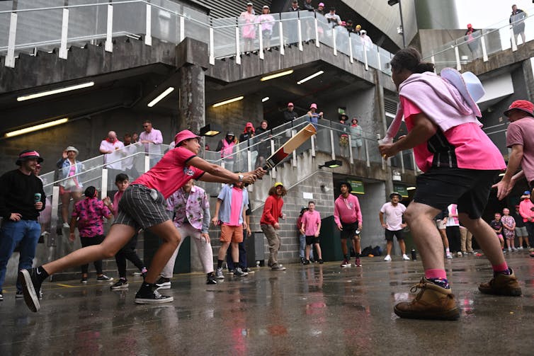 A group of cricket fans play an impromptu game of cricket in the rain on concrete outside the SCG.