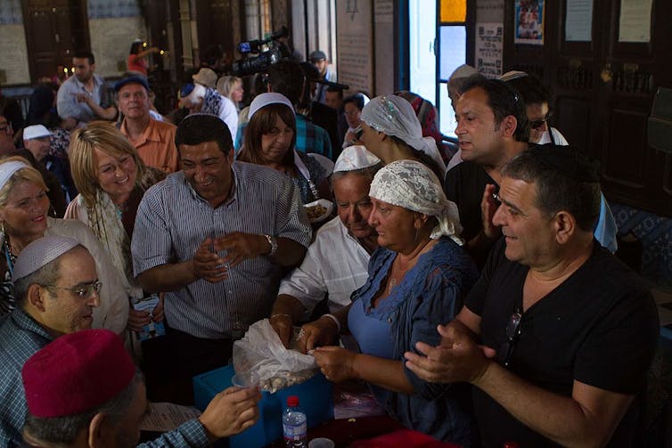 A crowd of people smile as they gather inside a building, many of them wearing white headcoverings.