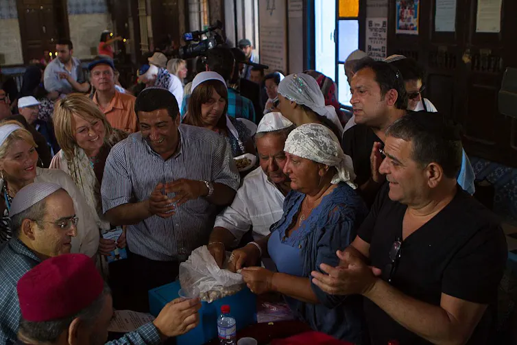 A crowd of people smile as they gather inside a building, many of them wearing white headcoverings.