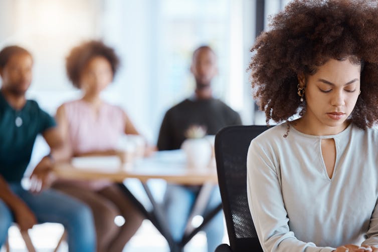 Woman sitting at a desk alone while a group of people sits together a short distance away