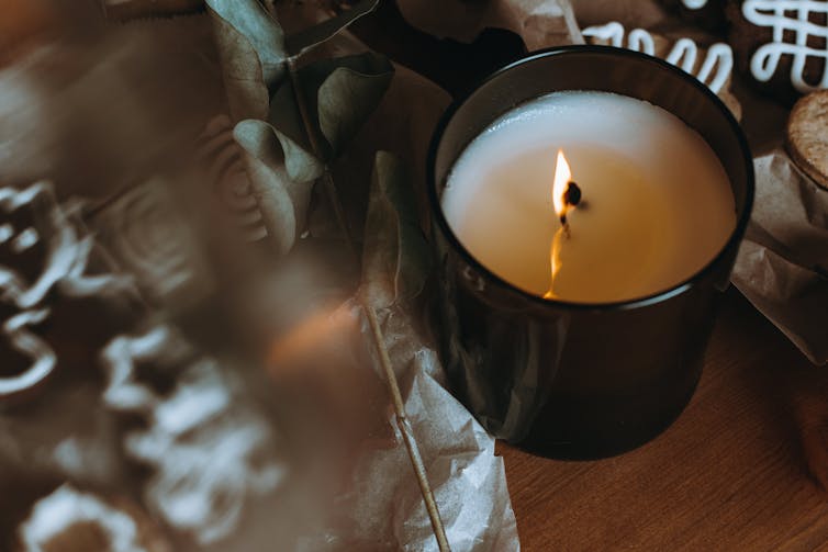 A candle burns in a glass jar, next to Christmas cookies.