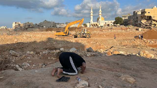 A man prays on his knees amid rubble.
