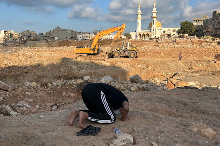 A man prays on his knees amid rubble.