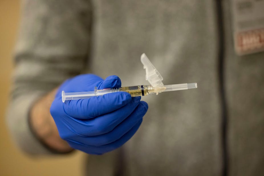A hand wearing a blue medical glove holds a syringe.