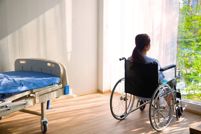 Woman in a wheelchair looking out of a large window