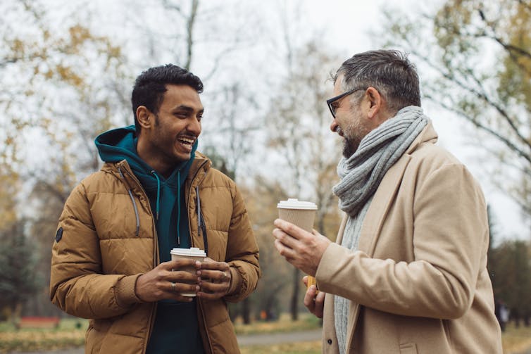 A young man and older man walking and talking with takeaway coffee cups