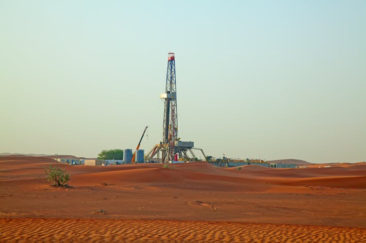 An oil drilling platform rising above red desert sand.