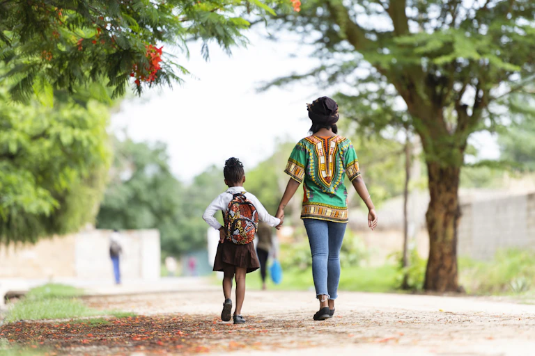 Back view of woman walking alongside a young girl in school uniform