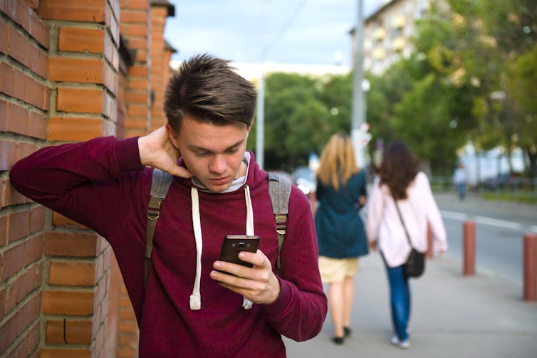 A young man seen looking at a phone while two women walk past.
