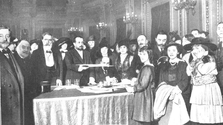 Un grupo de personas trajeadas miran a la cámara situados tras una mesa.