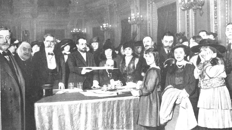 Un grupo de personas trajeadas miran a la cámara situados tras una mesa.