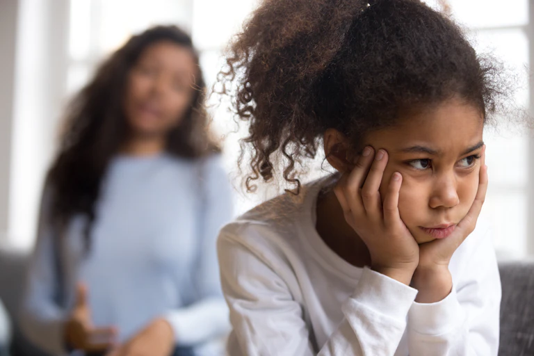 Grumpy girl sits in front of mother