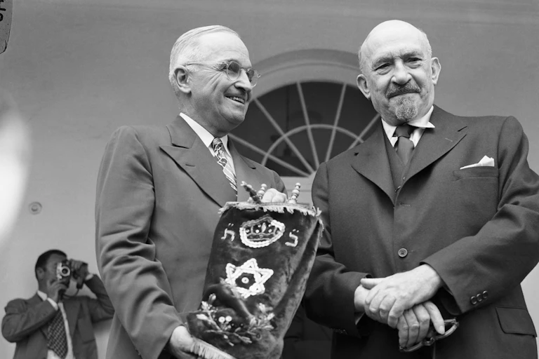 Two men in suits stand, one holding a Torah.