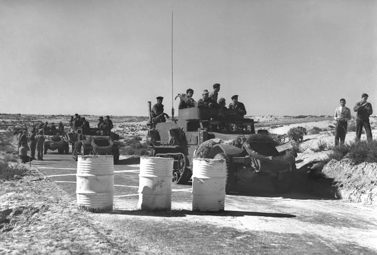 Soldiers, vehicles and barrels block a road.