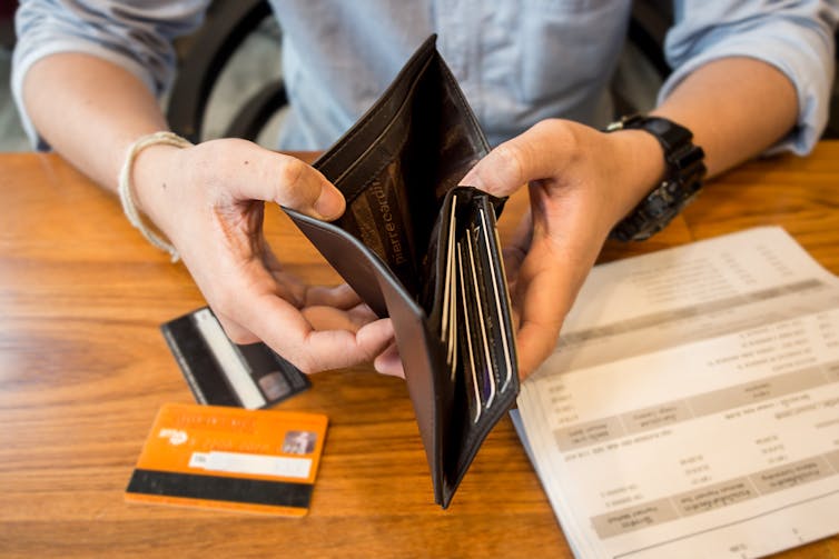Person holding empty wallet open, over credit cards and bills.
