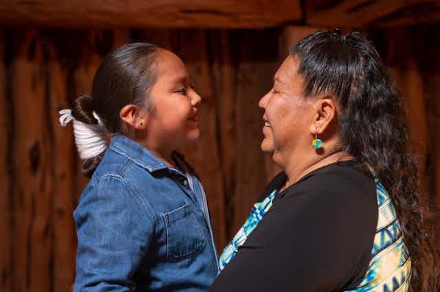 A Native American child (left) and older woman (right) embrace with smiles.
