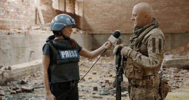 A female war correspondent interviews a man in a warzone
