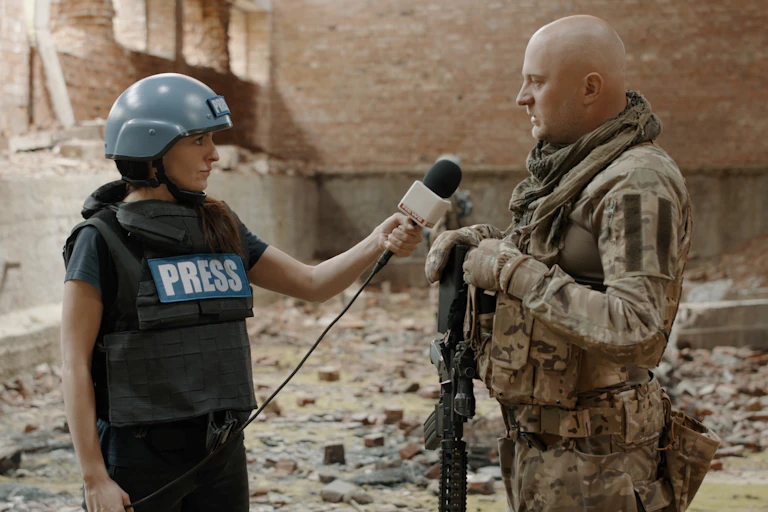 A female war correspondent interviews a man in a warzone