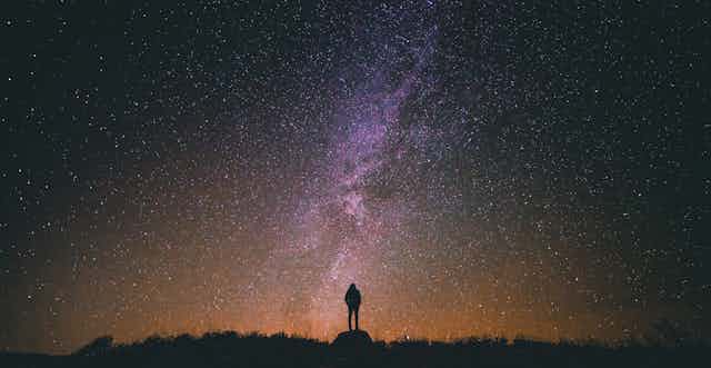 Photo of a person silhouetted against a starry sky.