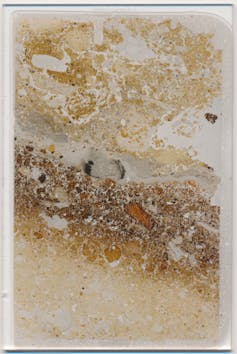 Photo of a thin slice of rock showing a dark band and traces of soot on a paler background.