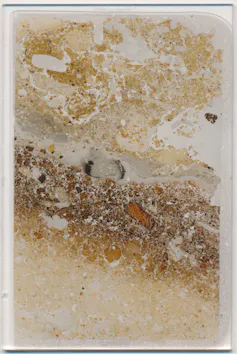 Photo of a thin slice of rock showing a dark band and traces of soot on a paler background.