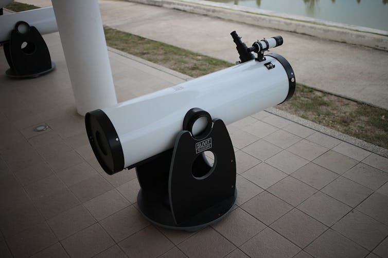 A white telescope on black sand sits on a tiled porch