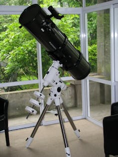 A large black telescope on a white mount sitting in a verandah