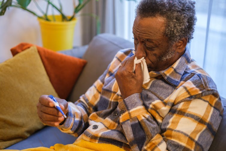 Man blows nose and looks at thermometre