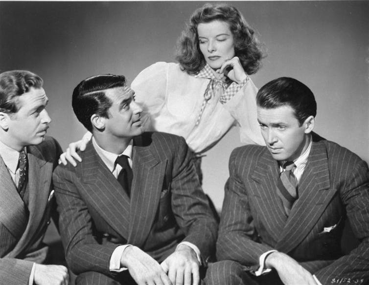 Katherine Hepburn looks down at three male actors in a black and white photo.