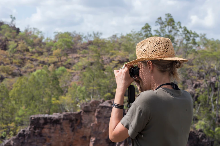 A woman in a sun hat looks at the view through a pair of binoculars near Jabiru in Kakadu National Park in Australia
